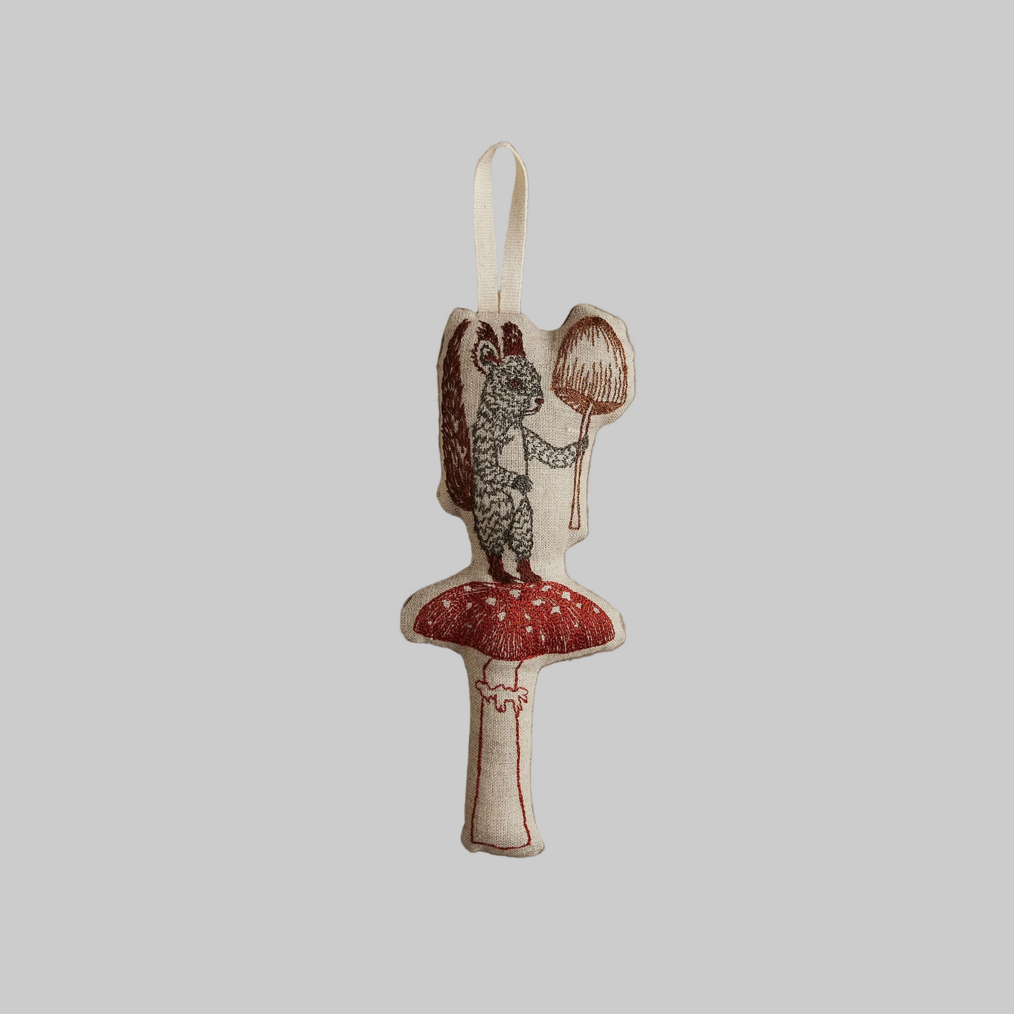 Coral and Tusk's "Squirrel with Mushroom" embroidered linen Christmas ornament featuring design of a squirrel standing on and holding a mushroom