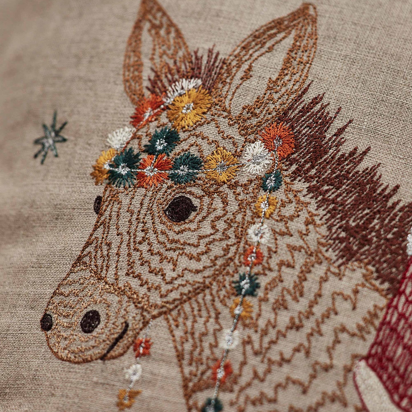 Coral and Tusk’s “Christmas Donkey” embroidered linen pillow featuring a fox dressed up as Santa riding in on a festively-adorned donkey, measures 16” x 16”