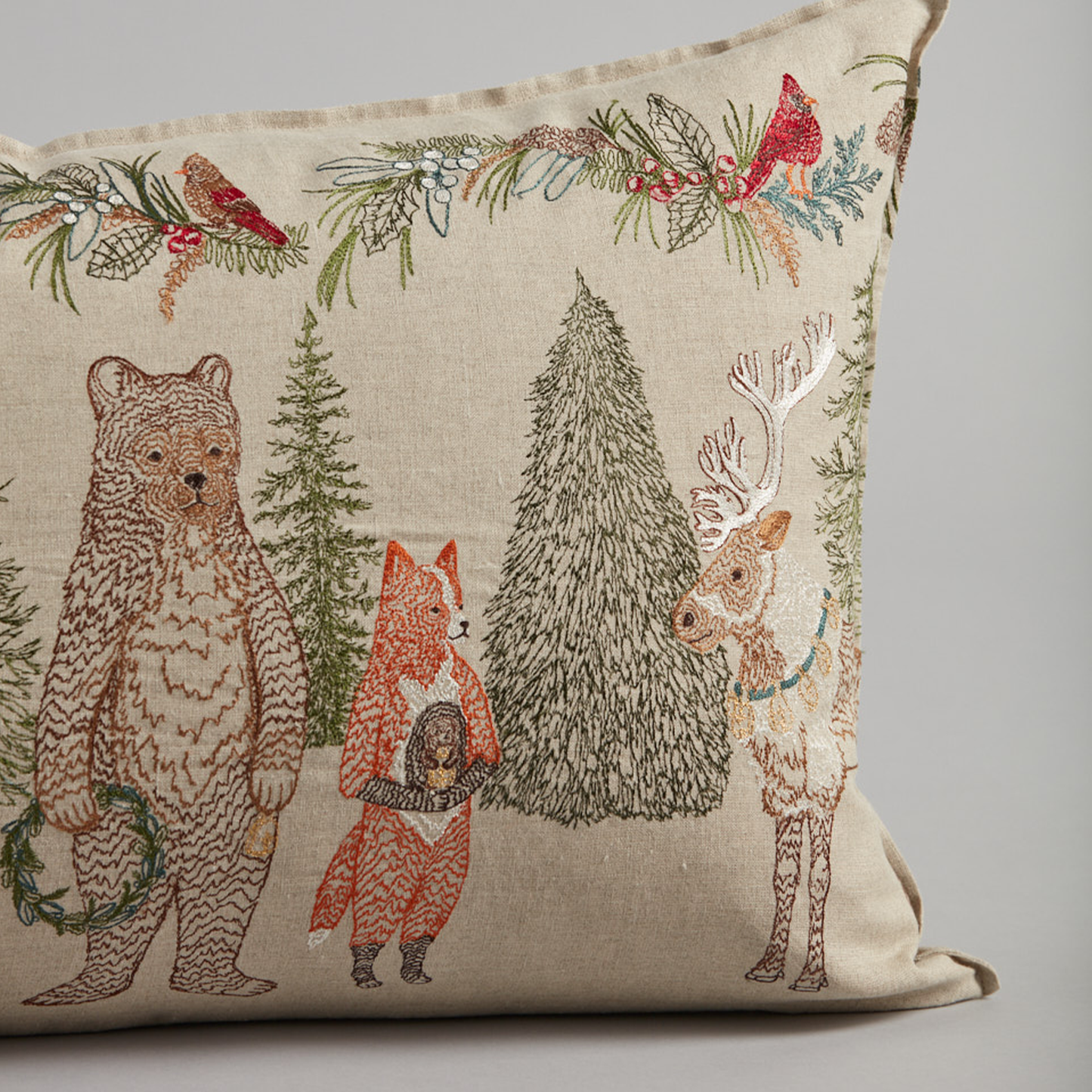 Coral and Tusk's "Christmas Cheer" embroidered linen lumbar pillow featuring festive woodland animals in an evergreen forest, measures 16" x 32"