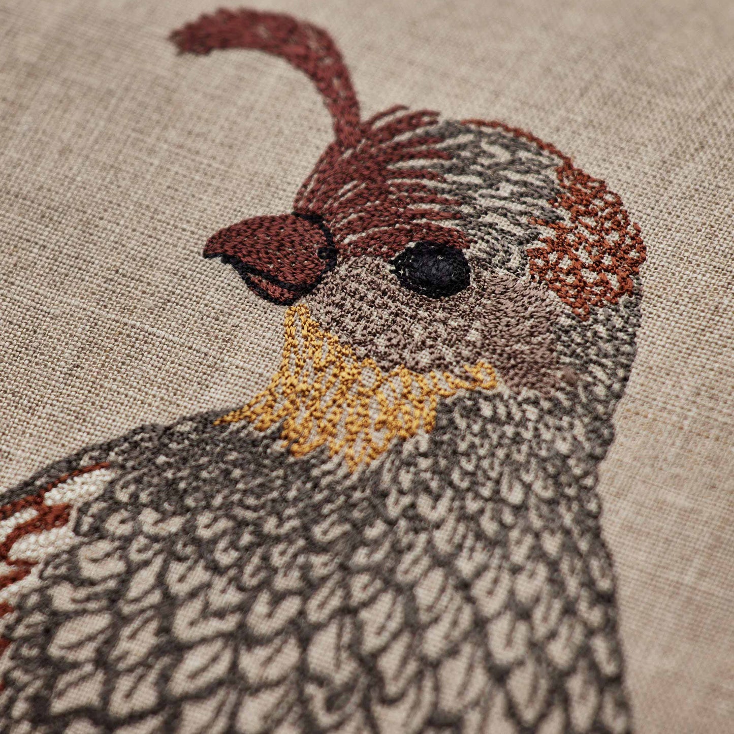Coral and Tusk’s “Desert Quail Love” embroidered linen pillow featuring a pair of quails with gold, brown, and gray feathers, measures 12” x 16”