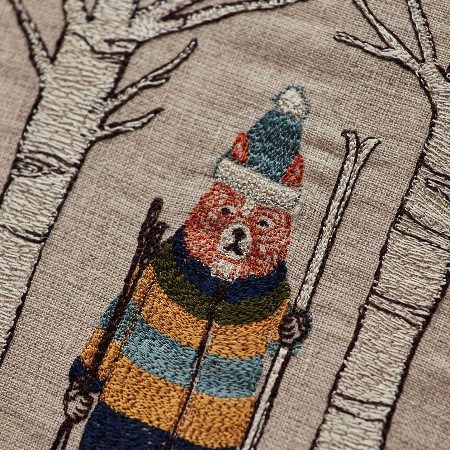Coral and Tusk’s “Aspen Skiers” embroidered linen pillow featuring fox and bunny skiers standing amongst aspen trees, measures 12” x 12”