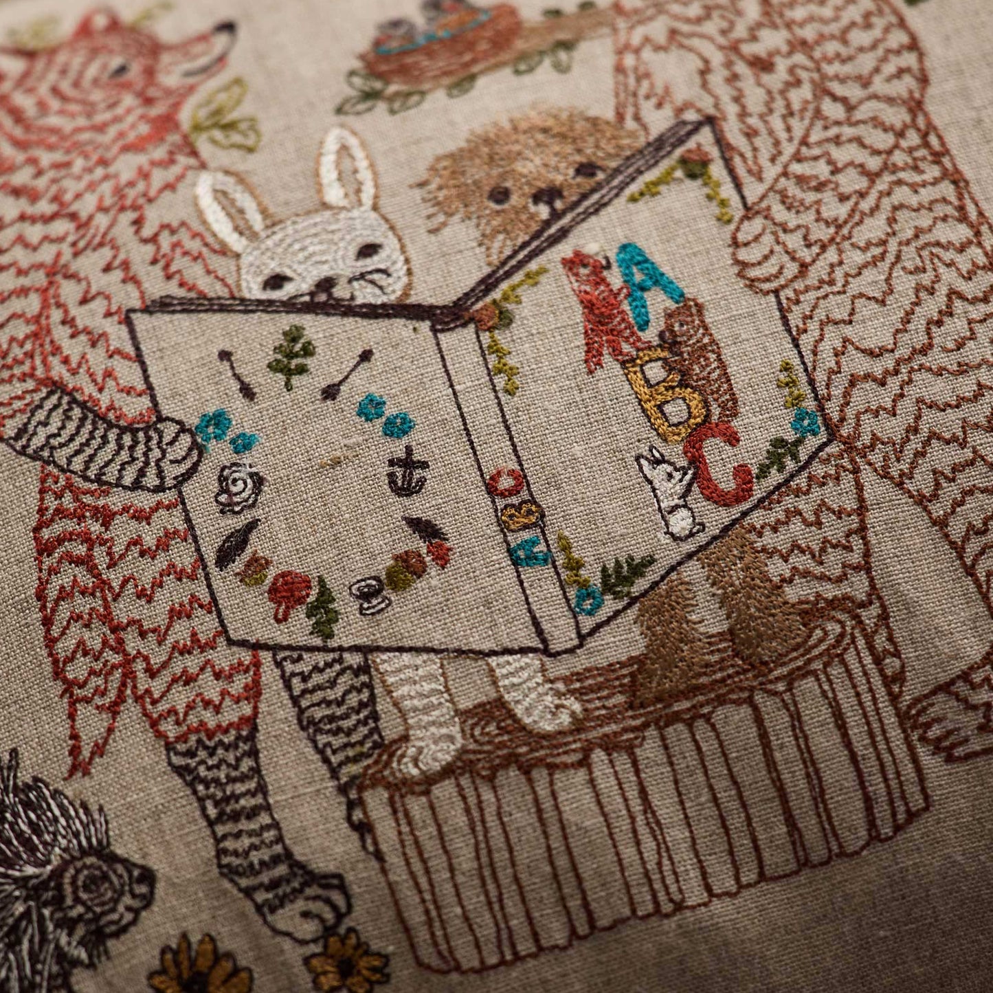 Coral and Tusk’s “Storytime” embroidered linen pillow featuring woodland animal friends gathered around listening to an A-B-C book be read aloud