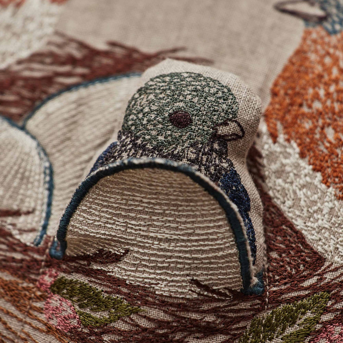 Coral and Tusk’s “Bluebird Nest” embroidered linen pocket pillow featuring a family of bluebirds in a cherry blossom tree, measures 12” x 16”