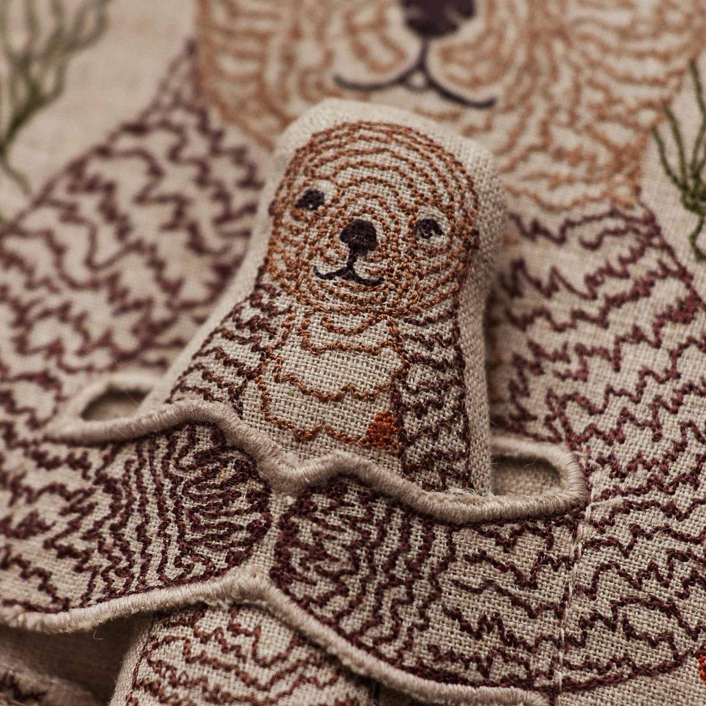 Coral and Tusk’s “Otter Mama” embroidered linen pocket pillow featuring a mother sea otter holding her pup in a sea of kelp