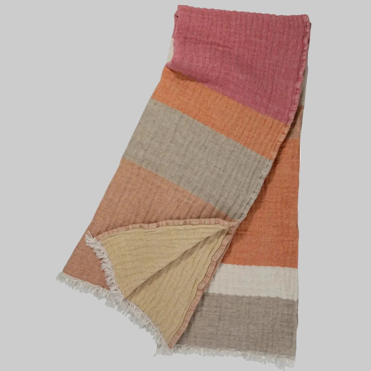Johanna Howard Home's woven Cozi Throw blanket in pink, orange, and tan, made of cotton, wool, and nylon.