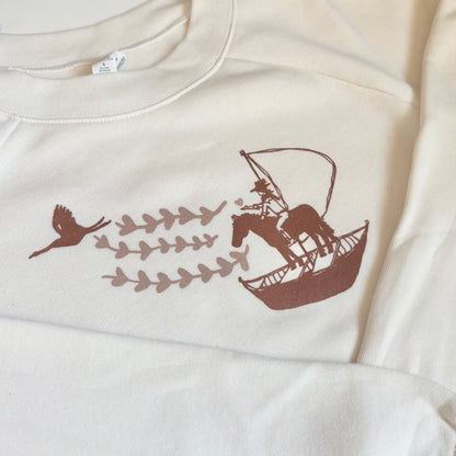 White sweatshirt with brown graphic design of a horse on a boat with birds and leaves.