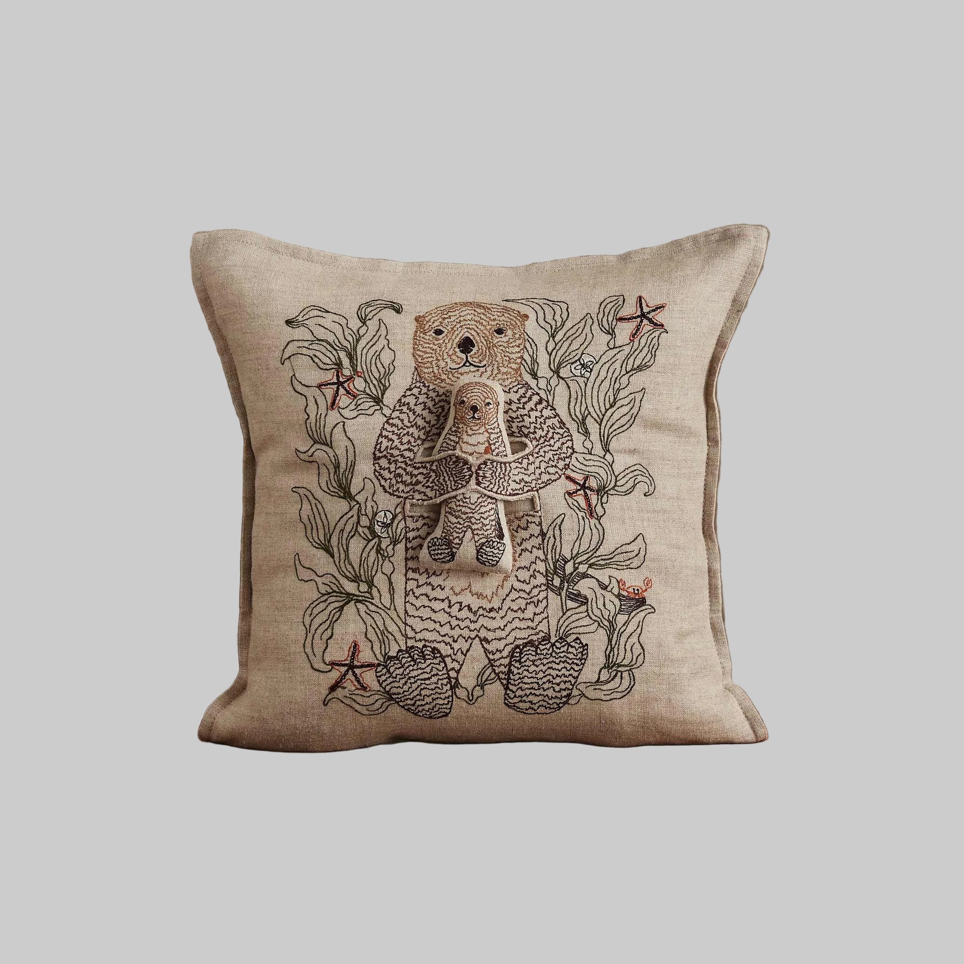 Coral and Tusk’s “Otter Mama” embroidered linen pocket pillow featuring a mother sea otter holding her pup in a sea of kelp