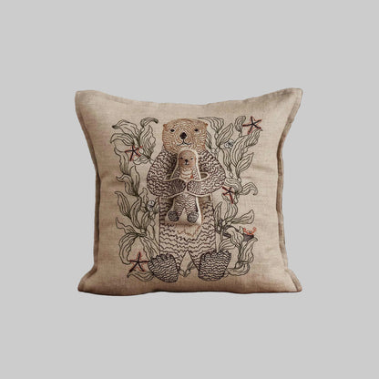 Coral and Tusk’s “Otter Mama” embroidered linen pocket pillow featuring a mother sea otter holding her pup in a sea of kelp
