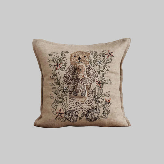 Coral and Tusk’s “Otter Mama” embroidered linen pocket pillow featuring a mother sea otter holding her pup in a sea of kelp