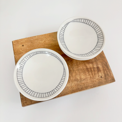 Two white ceramic dishes with black line stripe designs made by Jenny Dowd