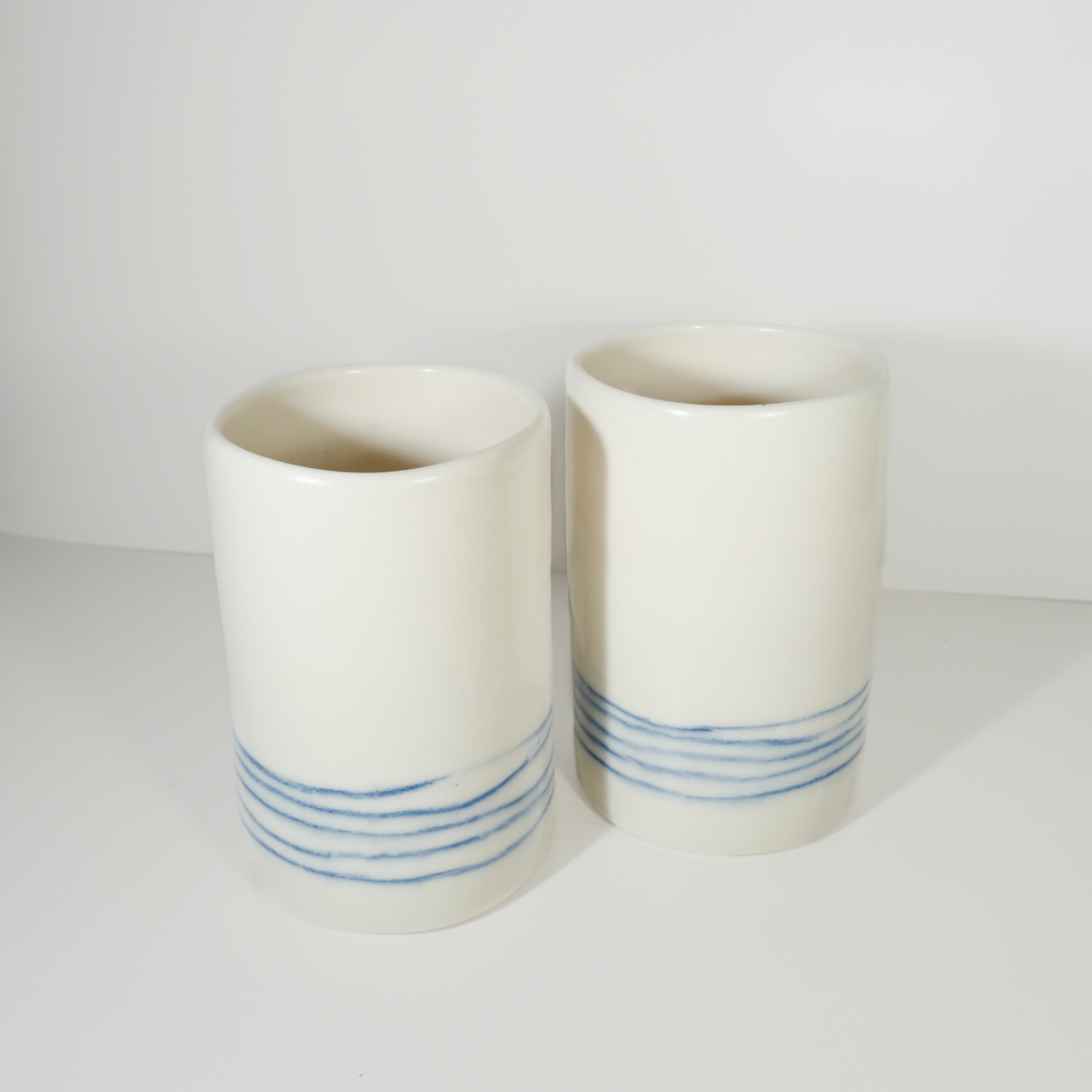 Two medium-sized white ceramic vases with blue line patterns on them, made by Jenny Dowd