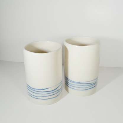 Two medium-sized white ceramic vases with blue line patterns on them, made by Jenny Dowd