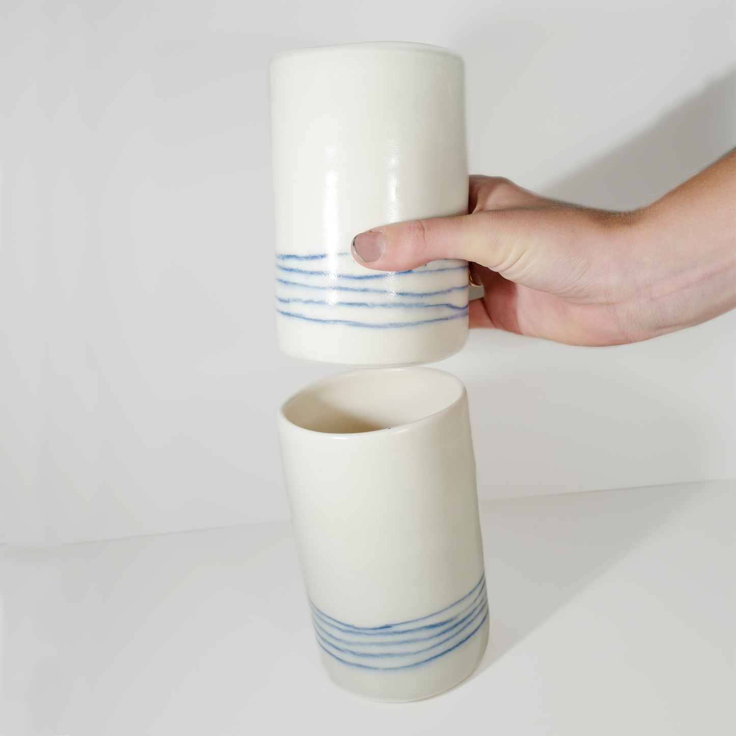 Two medium-sized white ceramic vases with blue line patterns on them, made by Jenny Dowd