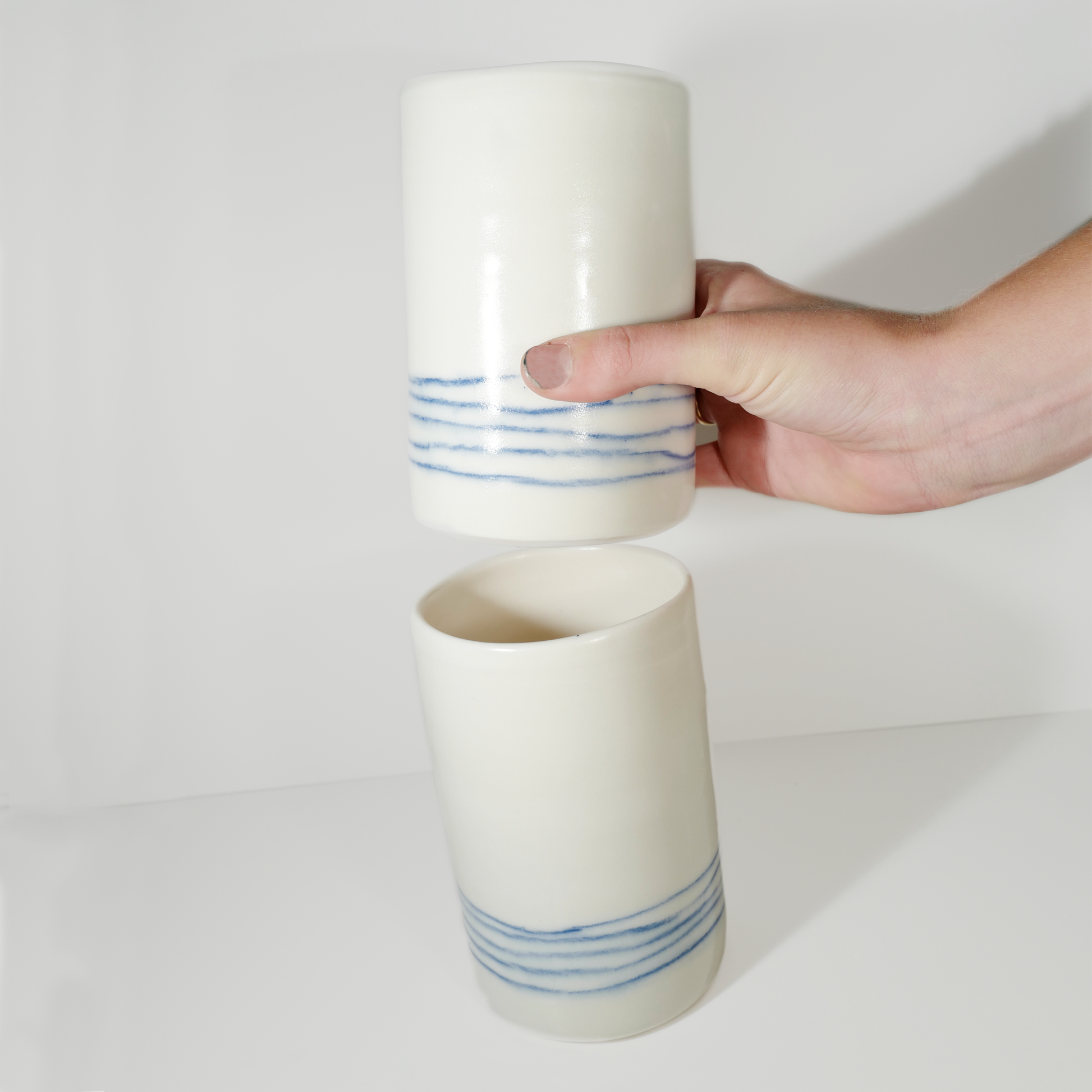 Two medium-sized white ceramic vases with blue line patterns on them, made by Jenny Dowd