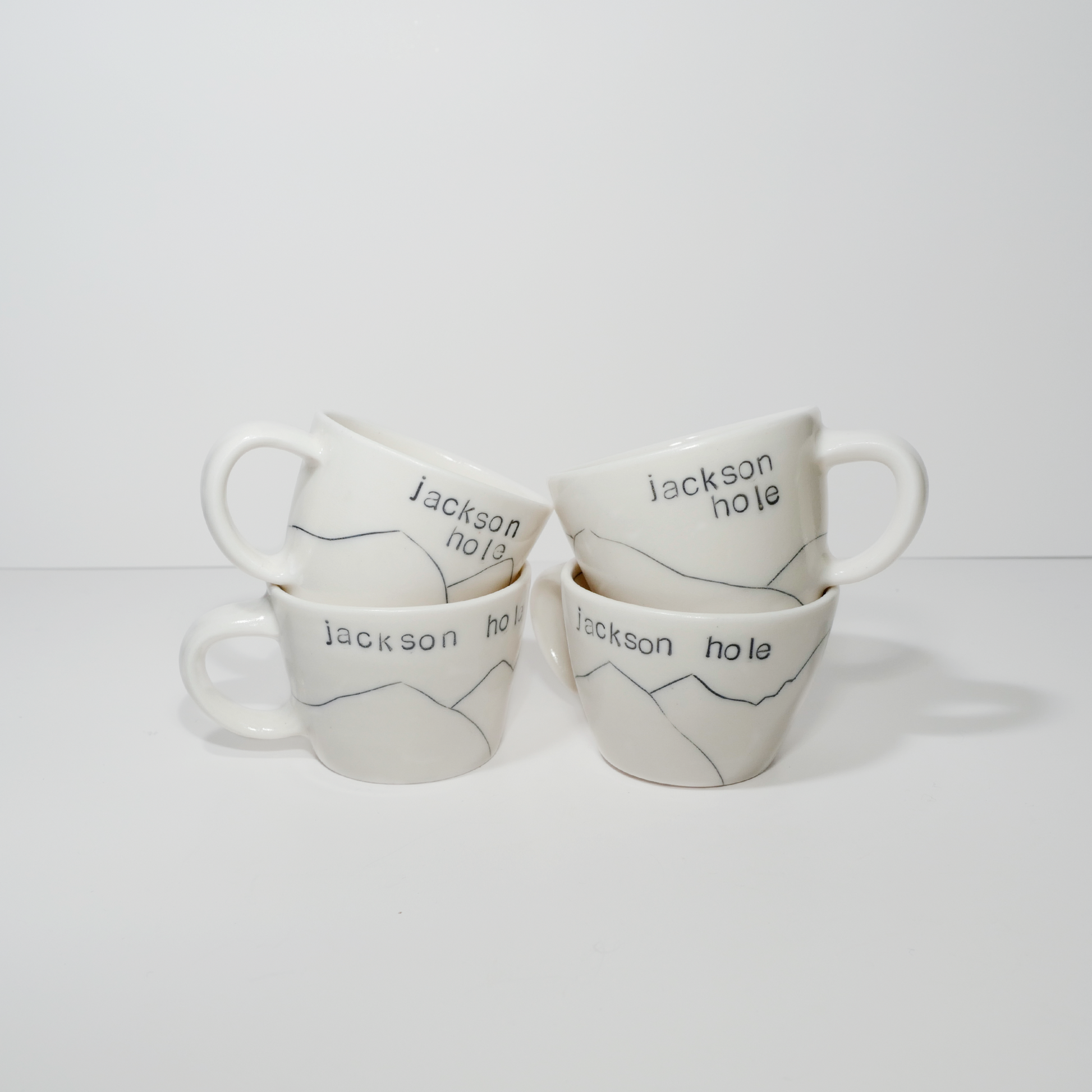 Four white ceramic espresso mugs with 'Jackson hole' text and a mountain design on them, made by Jenny Dowd