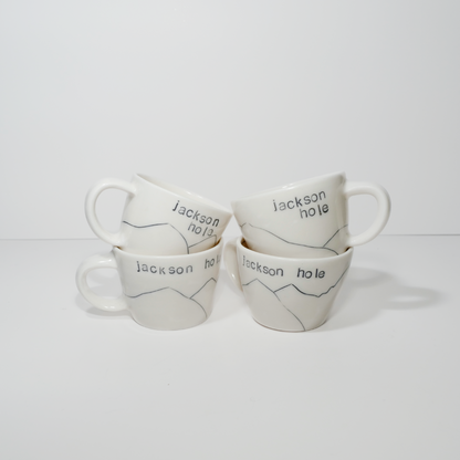 Four white ceramic espresso mugs with 'Jackson hole' text and a mountain design on them, made by Jenny Dowd