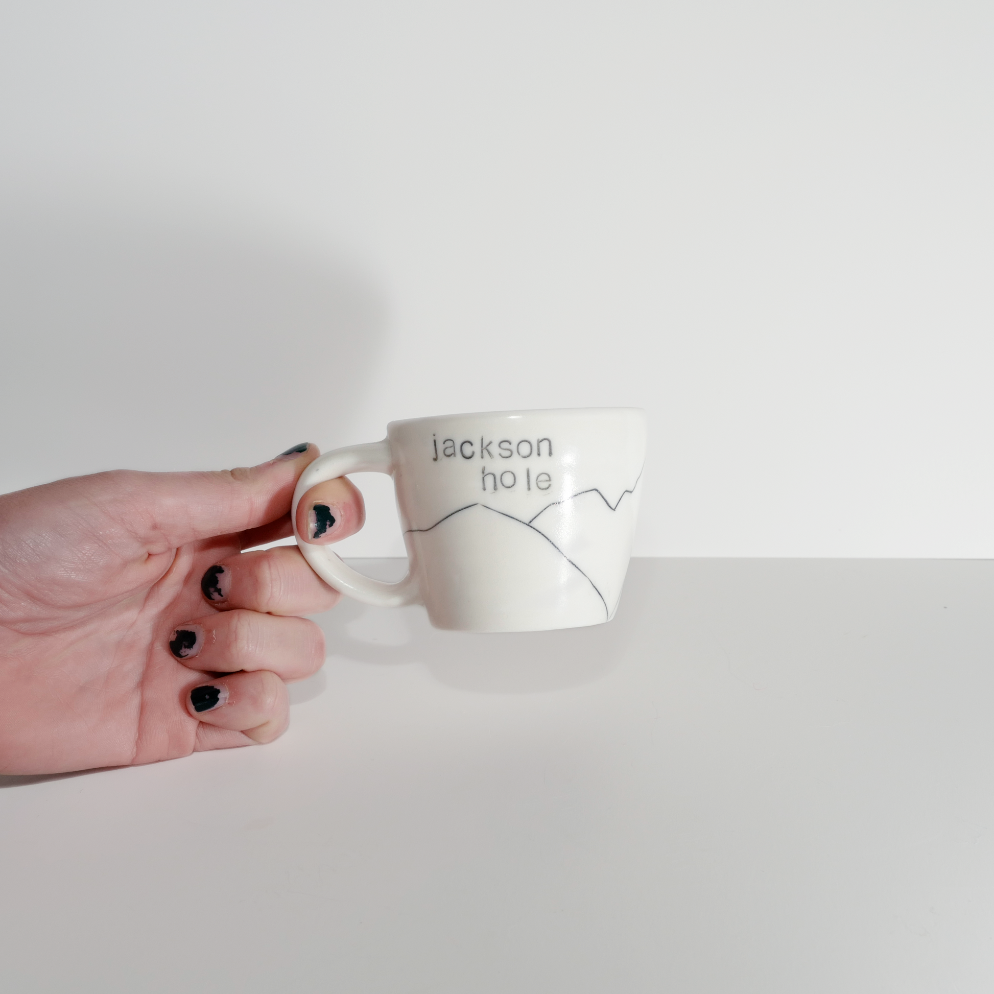 A white ceramic espresso mug with 'Jackson hole' text and a mountain design on them, made by Jenny Dowd