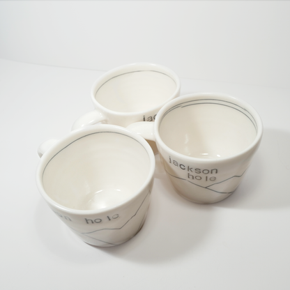 Three white ceramic espresso mugs with 'Jackson hole' text and a mountain design on them, made by Jenny Dowd