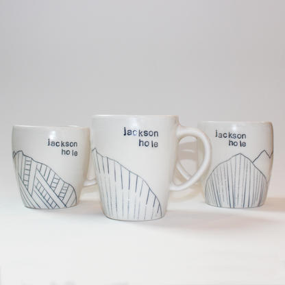 Three hand-thrown glazed porcelain mugs with 'Jackson Hole' text and mountain designs on them, made by Jenny Dowd