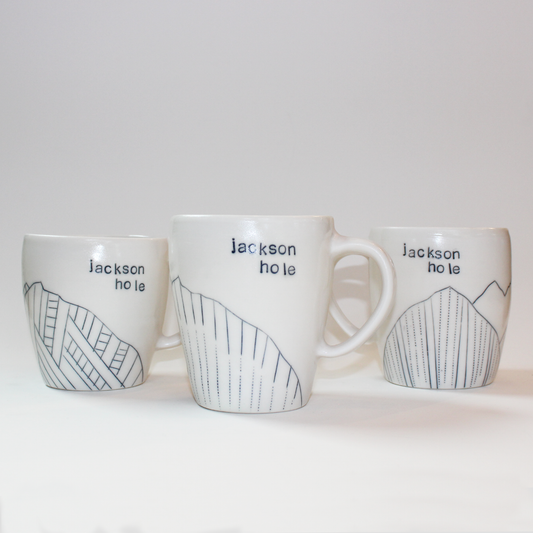 Three hand-thrown glazed porcelain mugs with 'Jackson Hole' text and mountain designs on them, made by Jenny Dowd