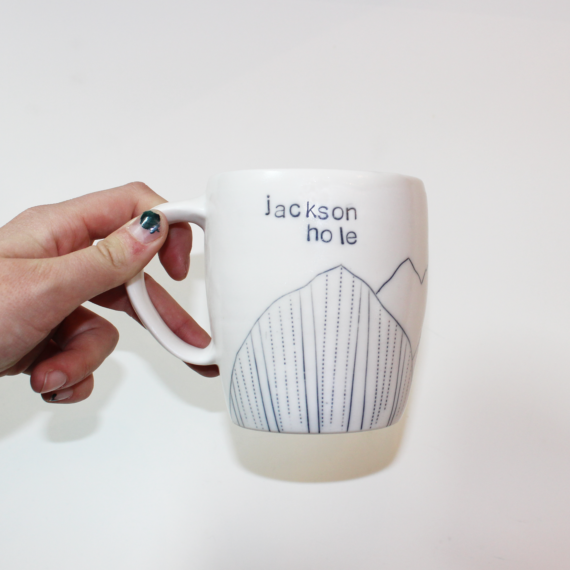 A hand-thrown glazed porcelain mug with 'Jackson Hole' text and mountain designs on them, made by Jenny Dowd