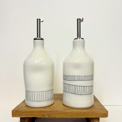 Two white ceramic oil cruet bottles with black line designs and silver nozzles 