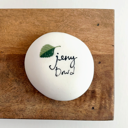 The bottom of a white ceramic dish with signature and green leaf details 
