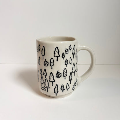 White mug with designs of black pine trees and cabins