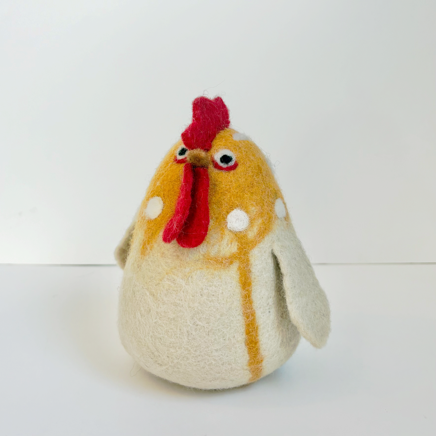 Golden felted chicken with white accents and a red comb on a white background