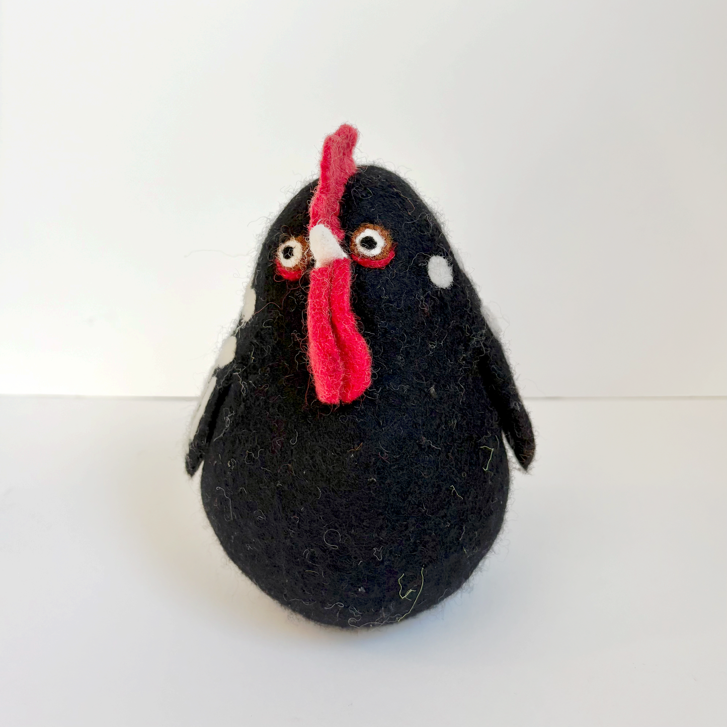 Black felted chicken with white spots and a red comb on a white background
