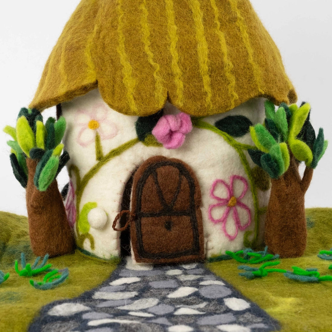 Close up of a felt cottage-style fairy house with a pointed green roof and small trees from The Winding Road
