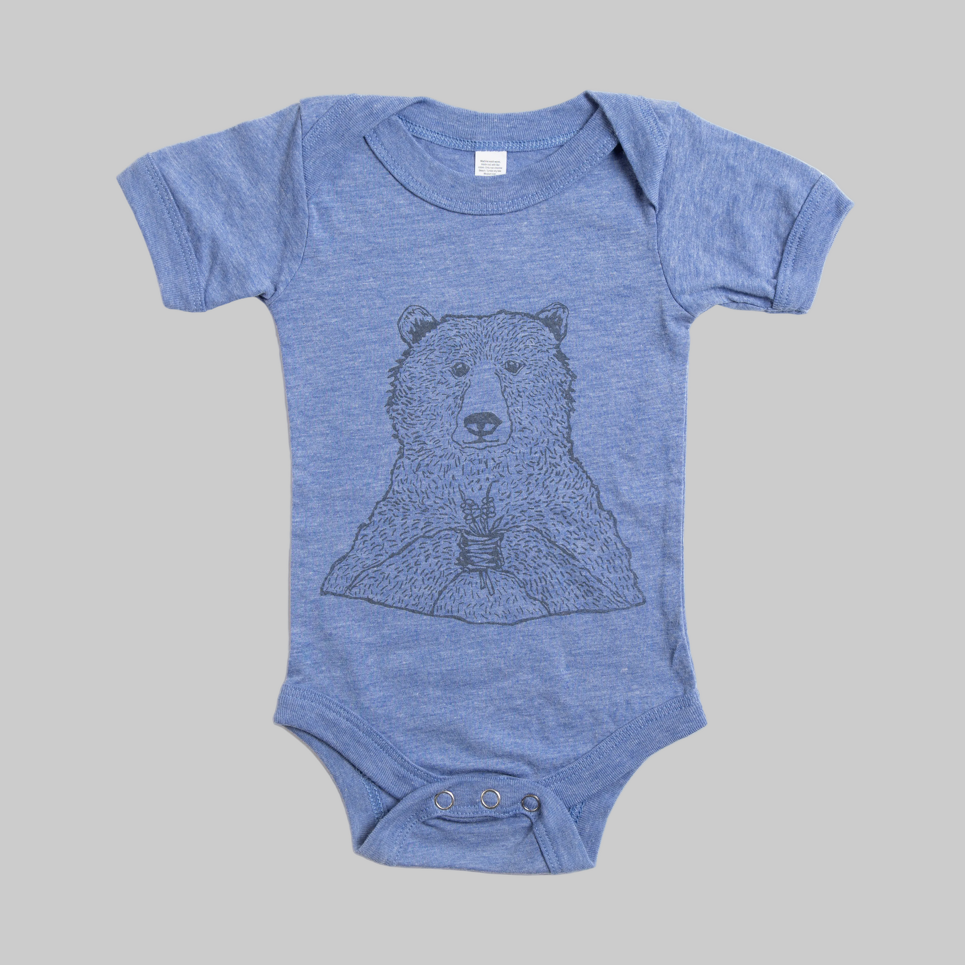 Bird and Buffalo’s baby onesie in blue with a bear holding flowers design, made locally in Jackson Hole, WY