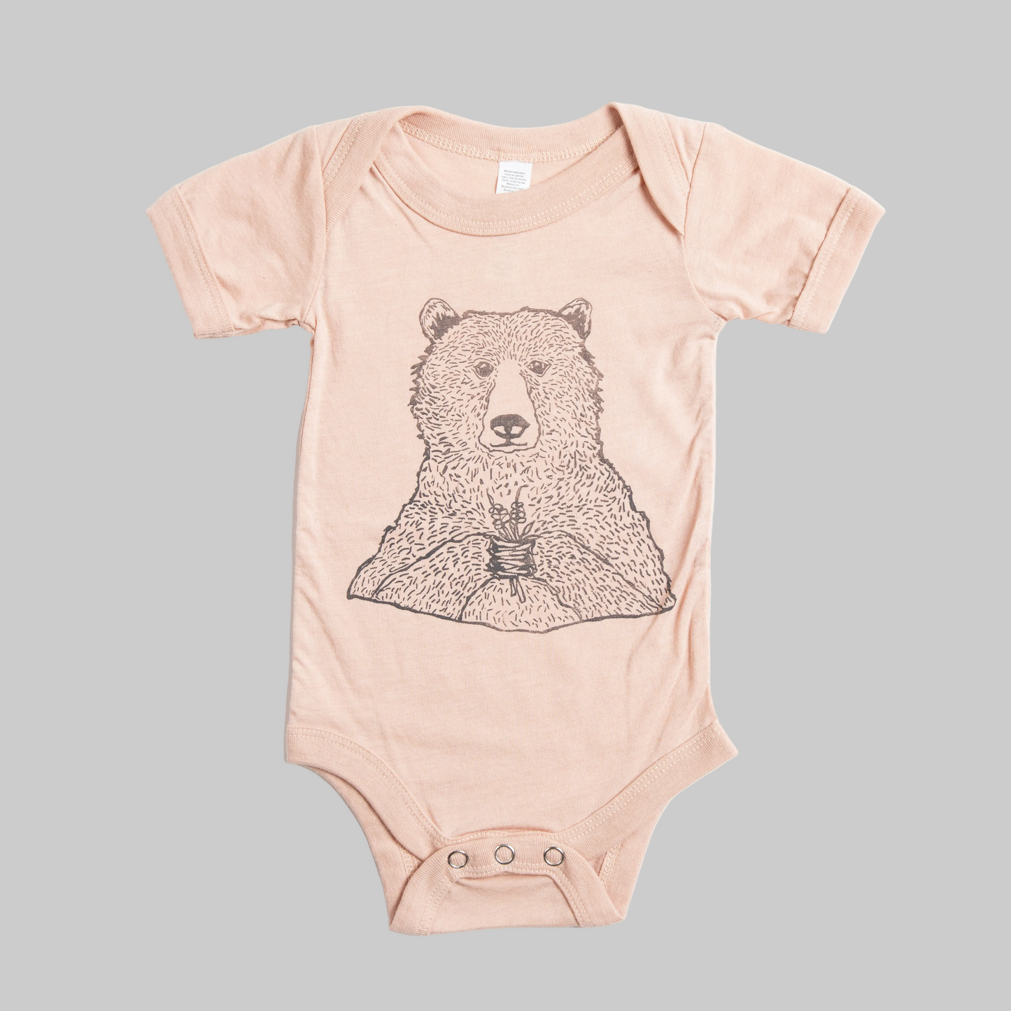 Bird and Buffalo’s baby onesie in pink with a bear holding flowers design, made locally in Jackson Hole, WY