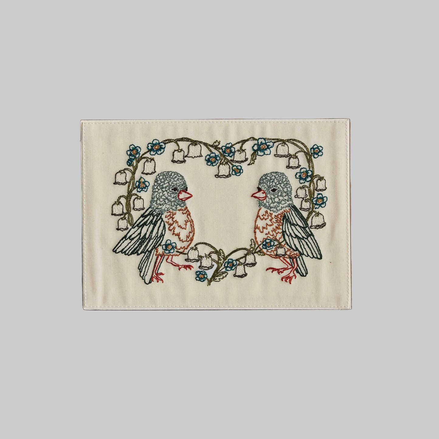 Coral and Tusk's "Lily Love Birds" embroidered keepsake card  featuring two birds sitting inside a heart-shaped floral wreath