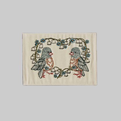 Coral and Tusk's "Lily Love Birds" embroidered keepsake card  featuring two birds sitting inside a heart-shaped floral wreath