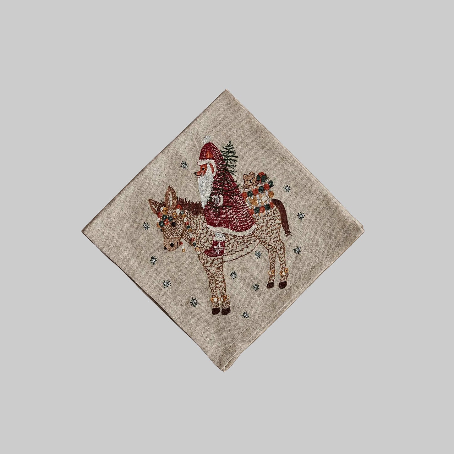 Coral and Tusk’s “Christmas Donkey” embroidered linen dinner napkin featuring a Santa fox carrying in presents on the back of a festive donkey
