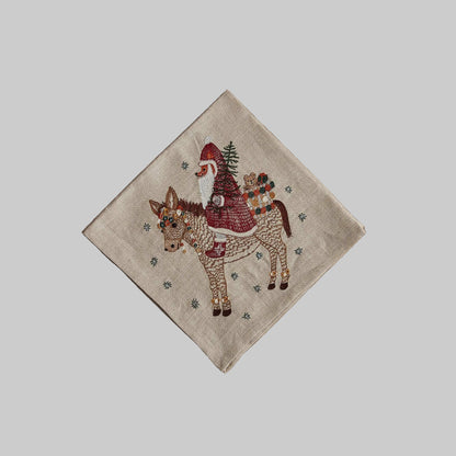 Coral and Tusk’s “Christmas Donkey” embroidered linen dinner napkin featuring a Santa fox carrying in presents on the back of a festive donkey