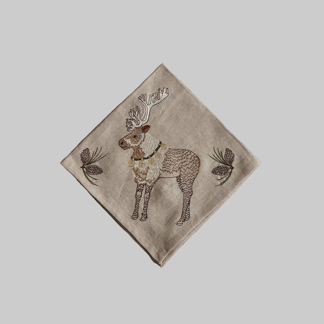 Coral and Tusk’s “Christmas Cheer Reindeer” embroidered linen dinner napkin featuring a reindeer with pinecones