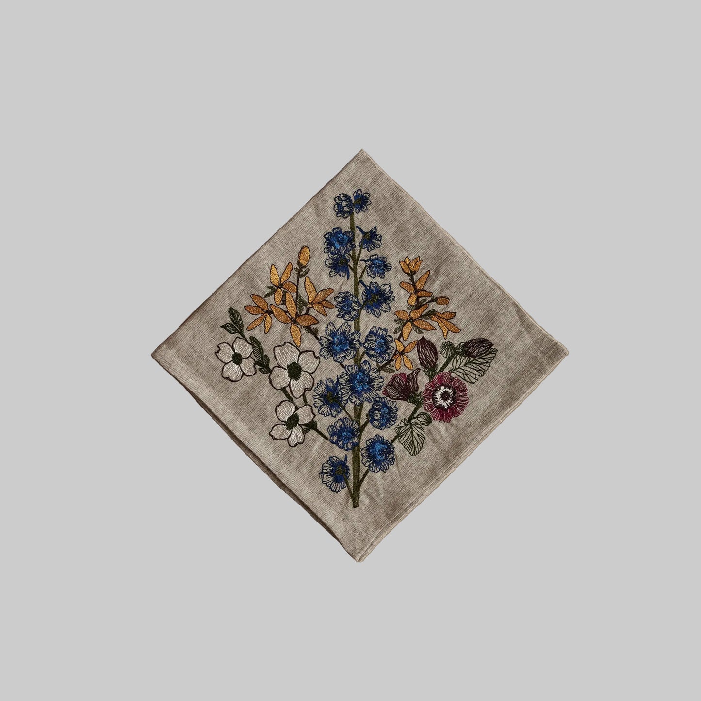 Coral and Tusk’s “Spring Stems” embroidered linen dinner napkin featuring a bouquet of blue, yellow, pink, and white florals