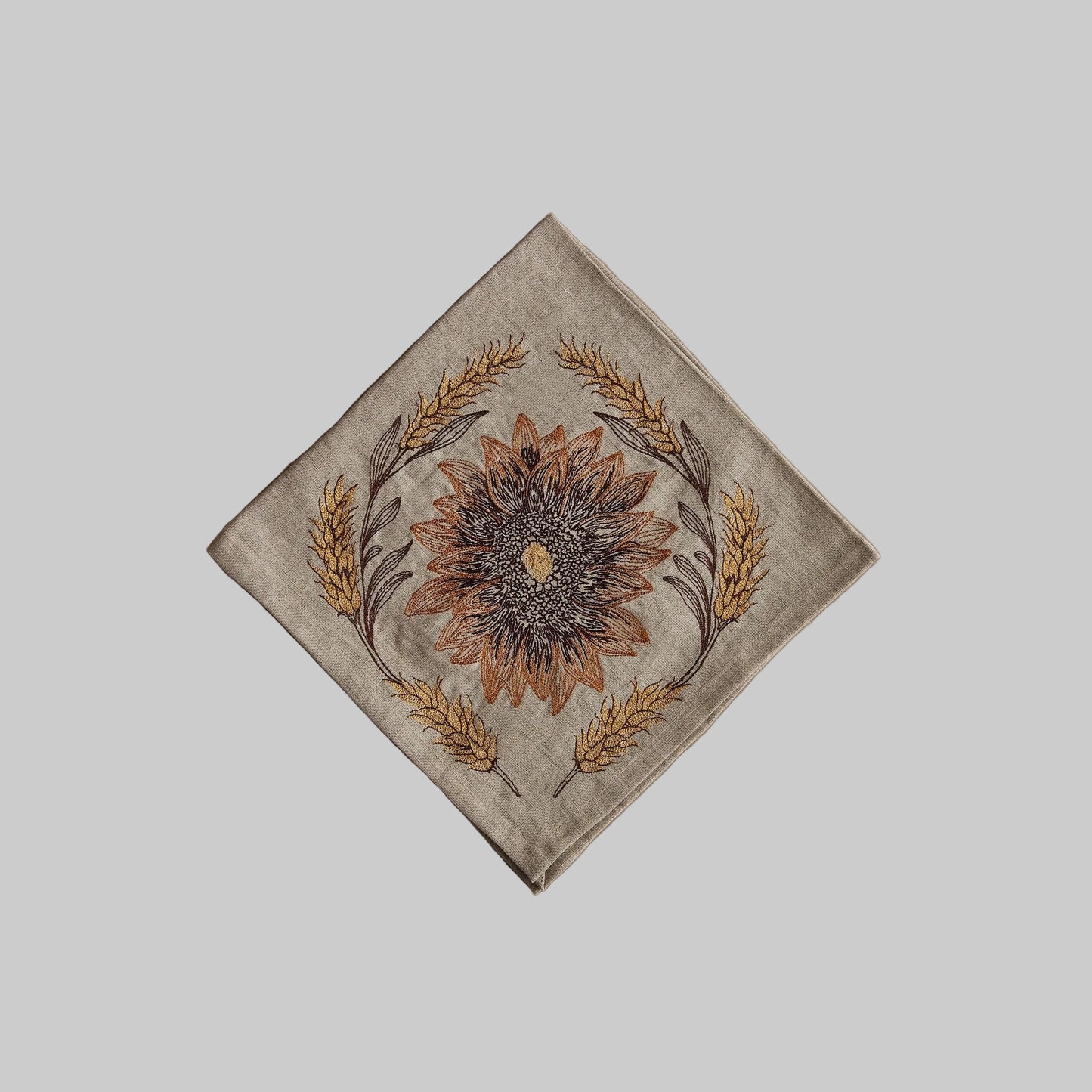 Coral and Tusk’s “Sunflower and Wheat” embroidered linen dinner napkin featuring a sunflower surrounded by strands of wheat