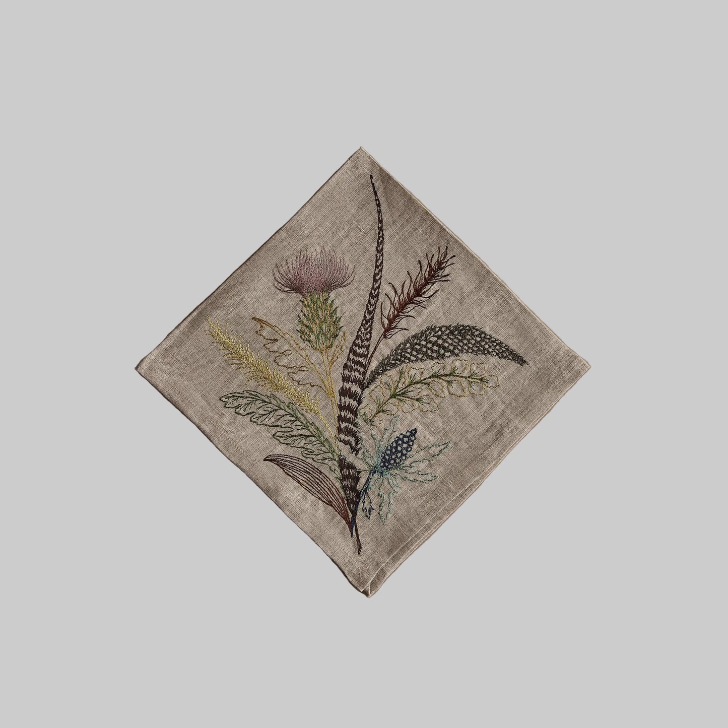 Coral and Tusk’s “Thistle” embroidered linen dinner napkin featuring a bouquet of leaves, grass, and thistles