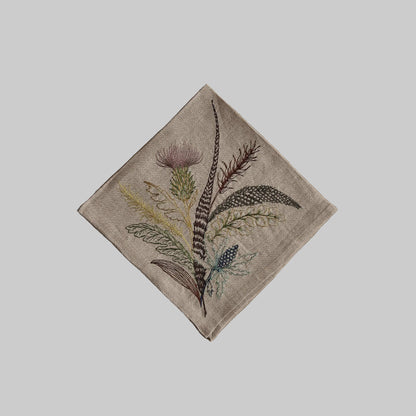 Coral and Tusk’s “Thistle” embroidered linen dinner napkin featuring a bouquet of leaves, grass, and thistles