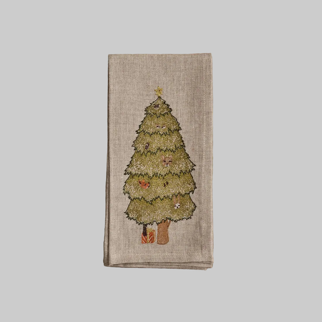 Coral and Tusk’s “Peek a Tree” embroidered linen dinner napkin featuring a Christmas tree with animal faces peeking through