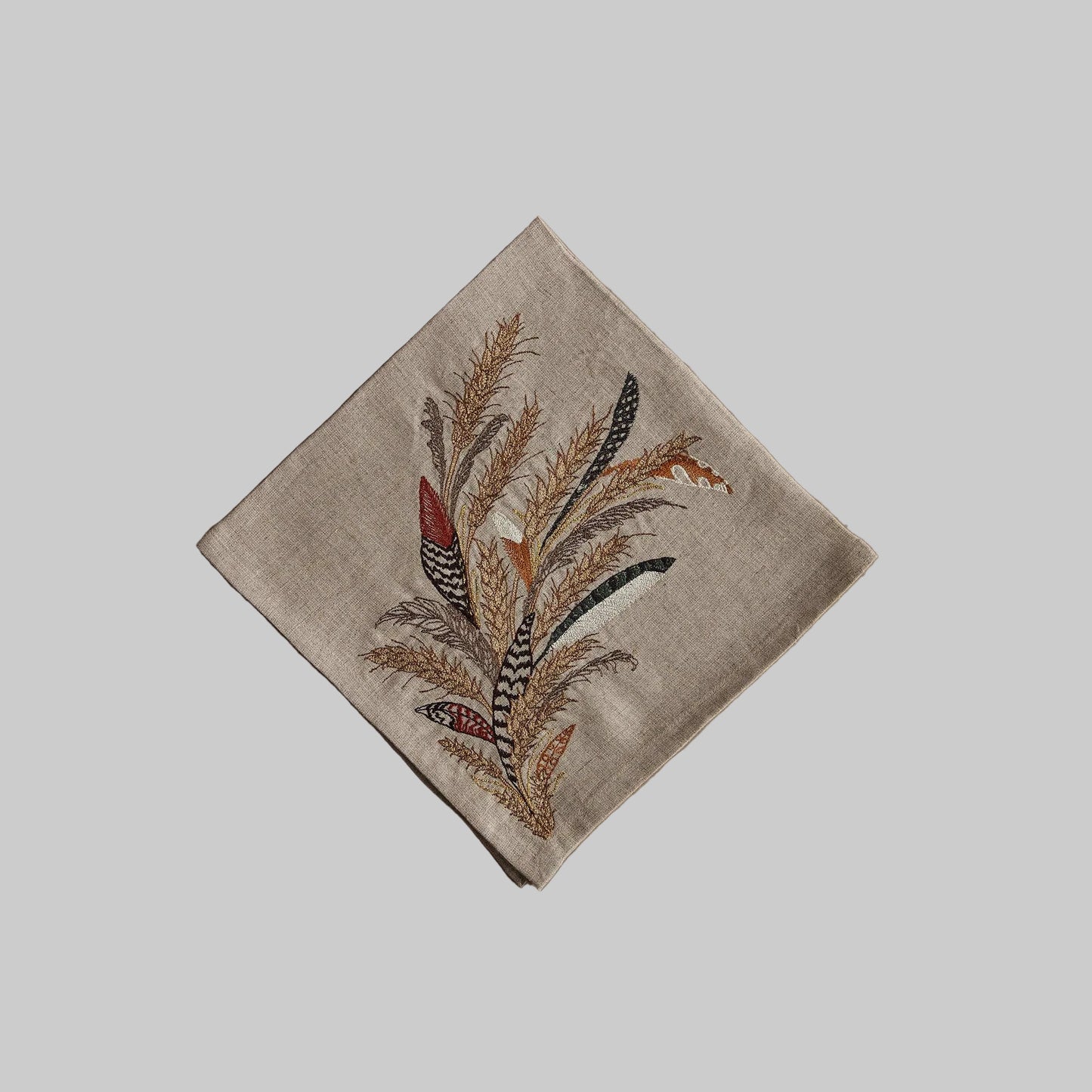 Coral and Tusk’s “Wheat Harvest” embroidered linen dinner napkin featuring a bouquet of grass, wheat strands, and found feathers