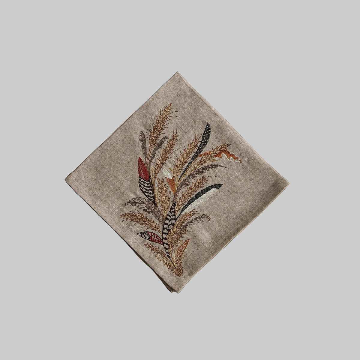 Coral and Tusk’s “Wheat Harvest” embroidered linen dinner napkin featuring a bouquet of grass, wheat strands, and found feathers
