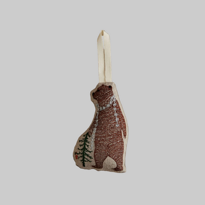 Coral and Tusk's "Bear with Tinsel" embroidered linen Christmas ornament featuring design of a bear standing next to a small tree wearing tinsel