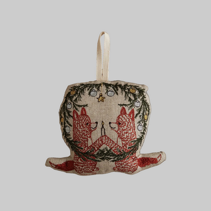 Coral and Tusk's "Togetherness Foxes" embroidered linen Christmas ornament featuring design of two foxes holding a candle surrounded by a festive wreath