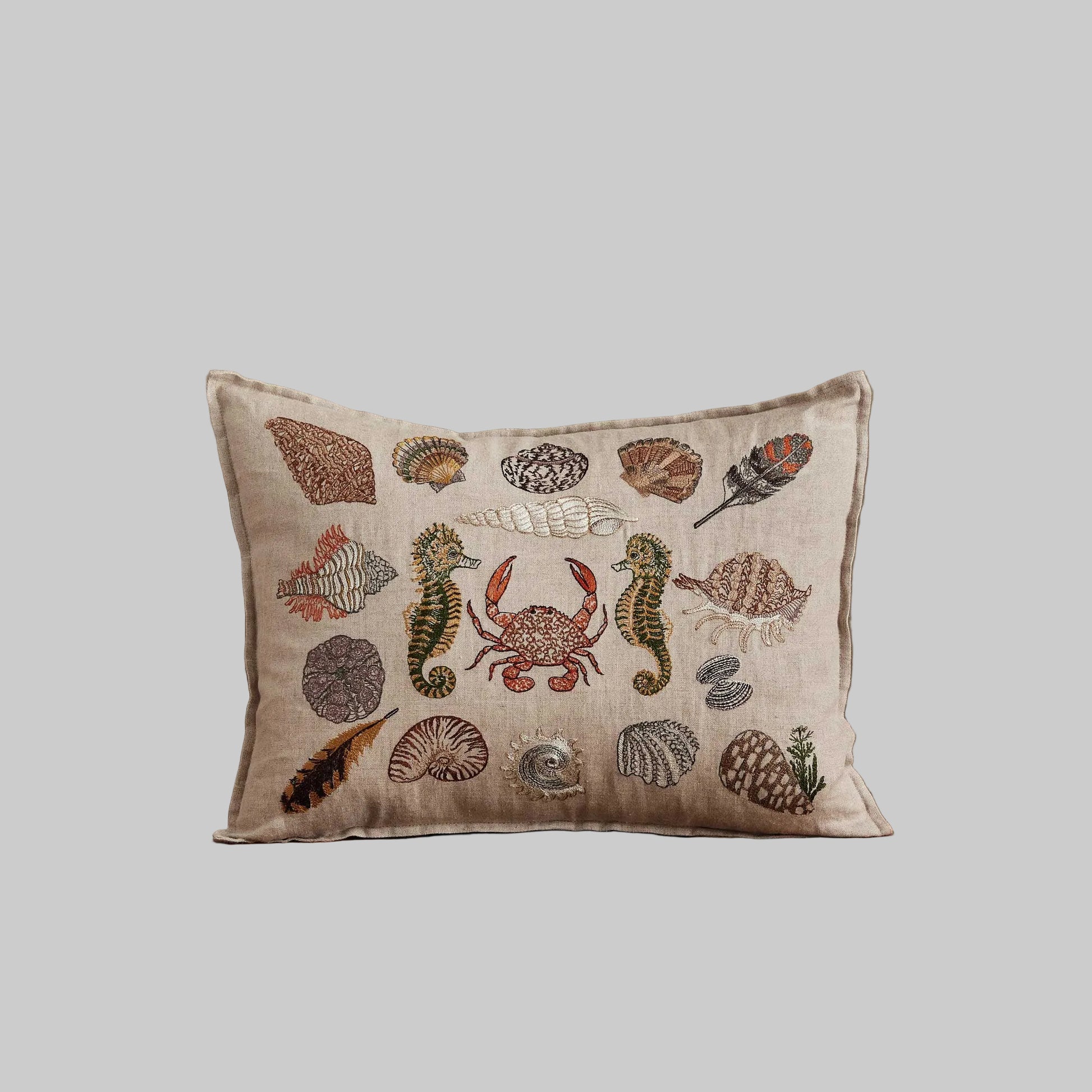 Coral and Tusk’s “Beach Walk” embroidered linen pillow featuring sea creatures and shells, measuring 12” x 16”