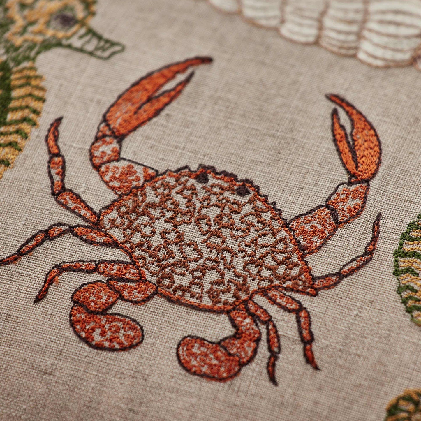 Coral and Tusk’s “Beach Walk” embroidered linen pillow featuring sea creatures and shells, measuring 12” x 16”