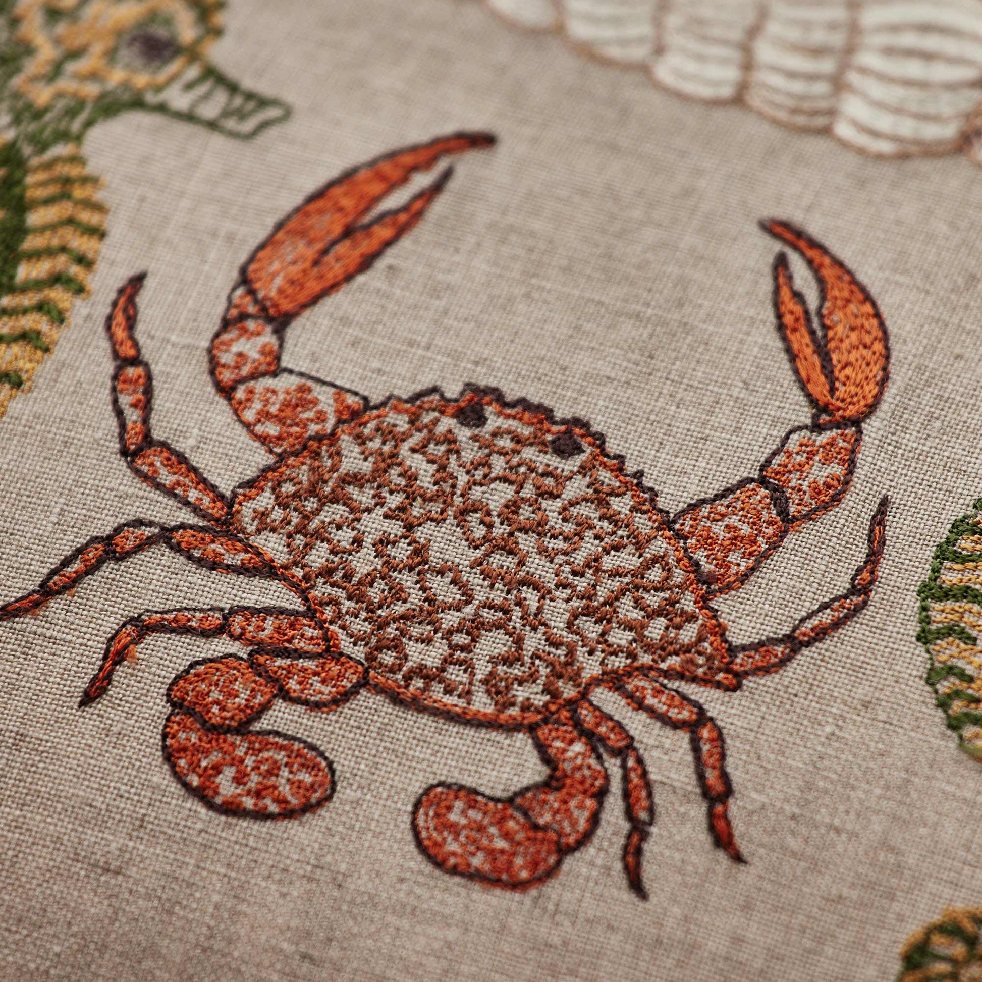 Coral and Tusk’s “Beach Walk” embroidered linen pillow featuring sea creatures and shells, measuring 12” x 16”